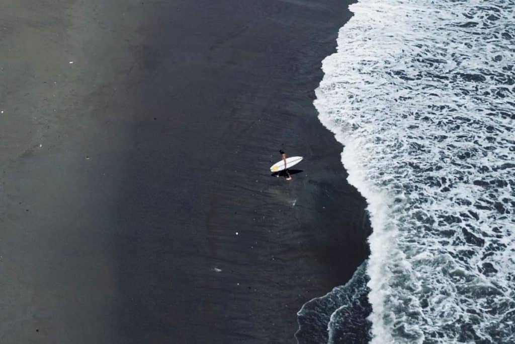 Drone shot of a surfer emerging from white and black waves