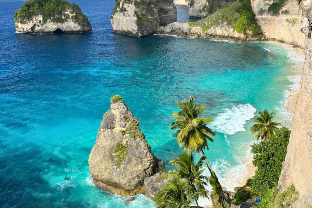 Crystal-clear turquoise waters and white sandy beach at Nusa Penida with dramatic cliffs in the background.