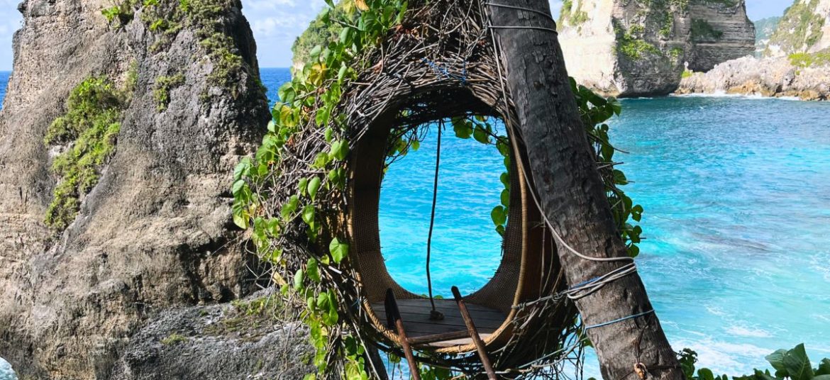 Wooden swings overlooking turquoise waters and dramatic cliffs at a beach in Nusa Penida.