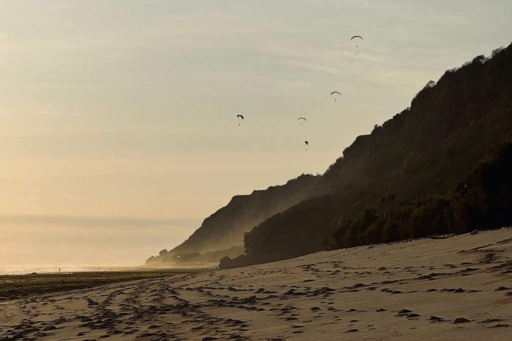 Paraglider soaring above Uluwatu cliffs at sunset