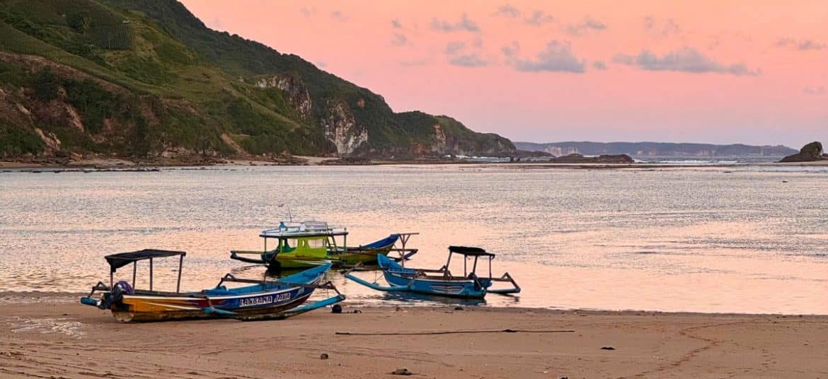 Vibrant sunset over the ocean with palm trees in Senggigi, West Lombok.