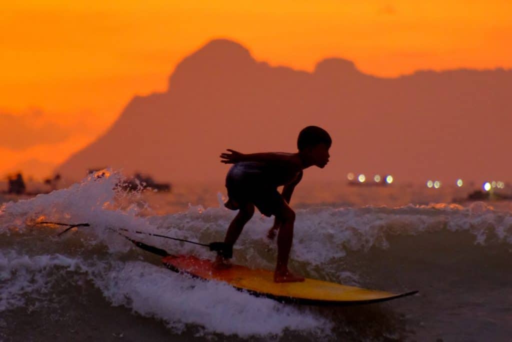 Kid surfing at sunset Lombok Indonesia with golden sky and ocean waves