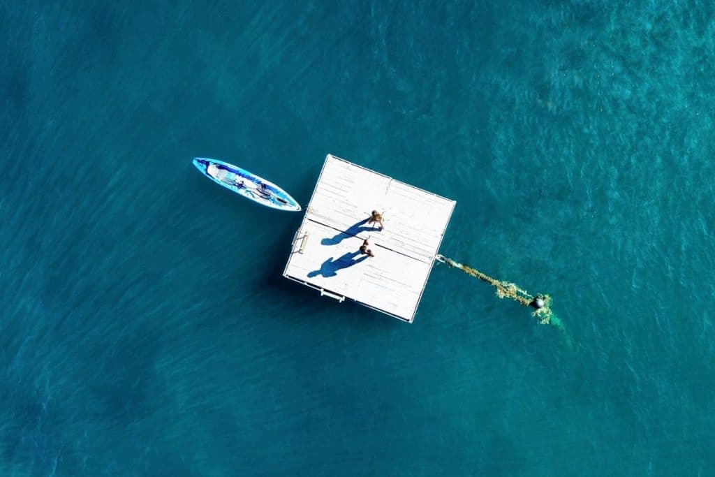 Two people kayaking through calm, clear waters with tropical hills in the distance in Komodo National Park.