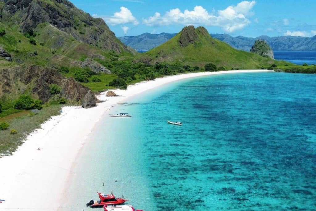 Traditional wooden boat cruising through the turquoise waters of Komodo National Park with hilly islands in the background.