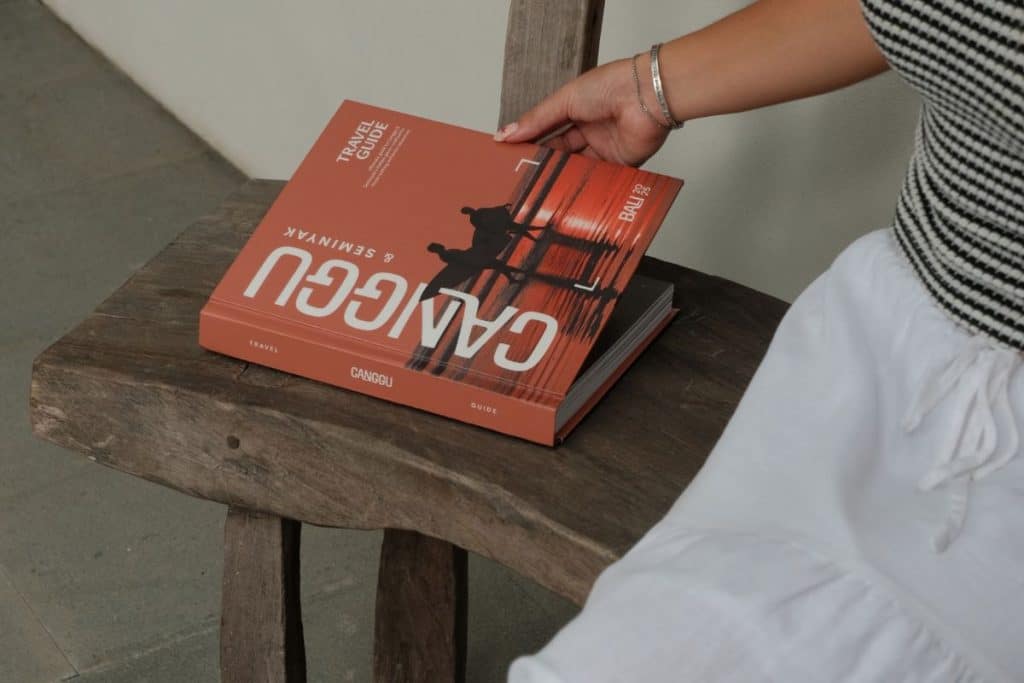 Person holding the Canggu & Seminyak Travel Guide while seated on a bench