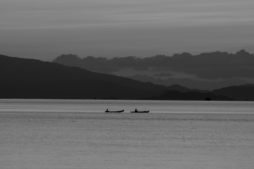 Two traditional wooden boats floating on calm water beneath a colourful sunset in Flores, Indonesia.