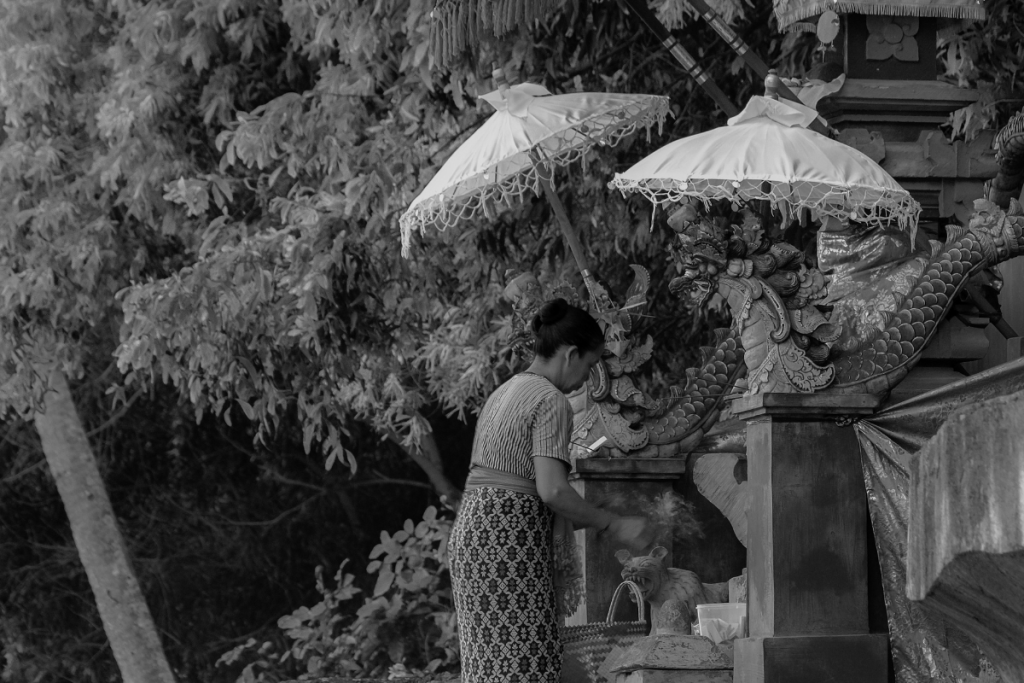 A Balinese woman placing an offering at an intricately carved temple shrine.