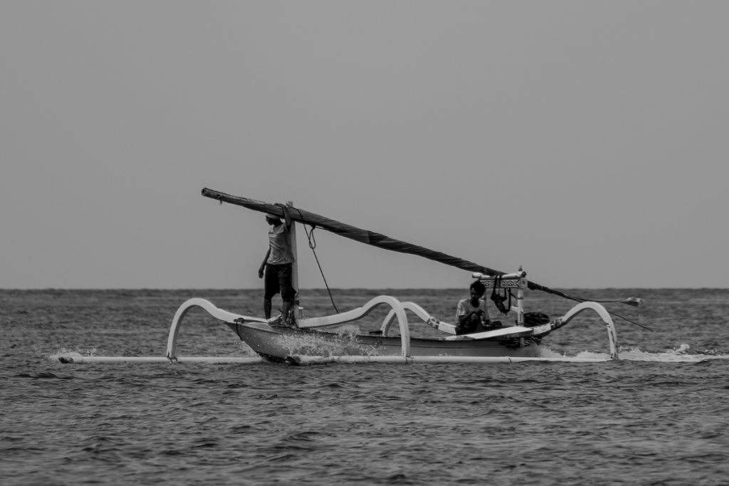 Two fishermen aboard a traditional wooden outrigger boat off the coast of Lombok, Indonesia.