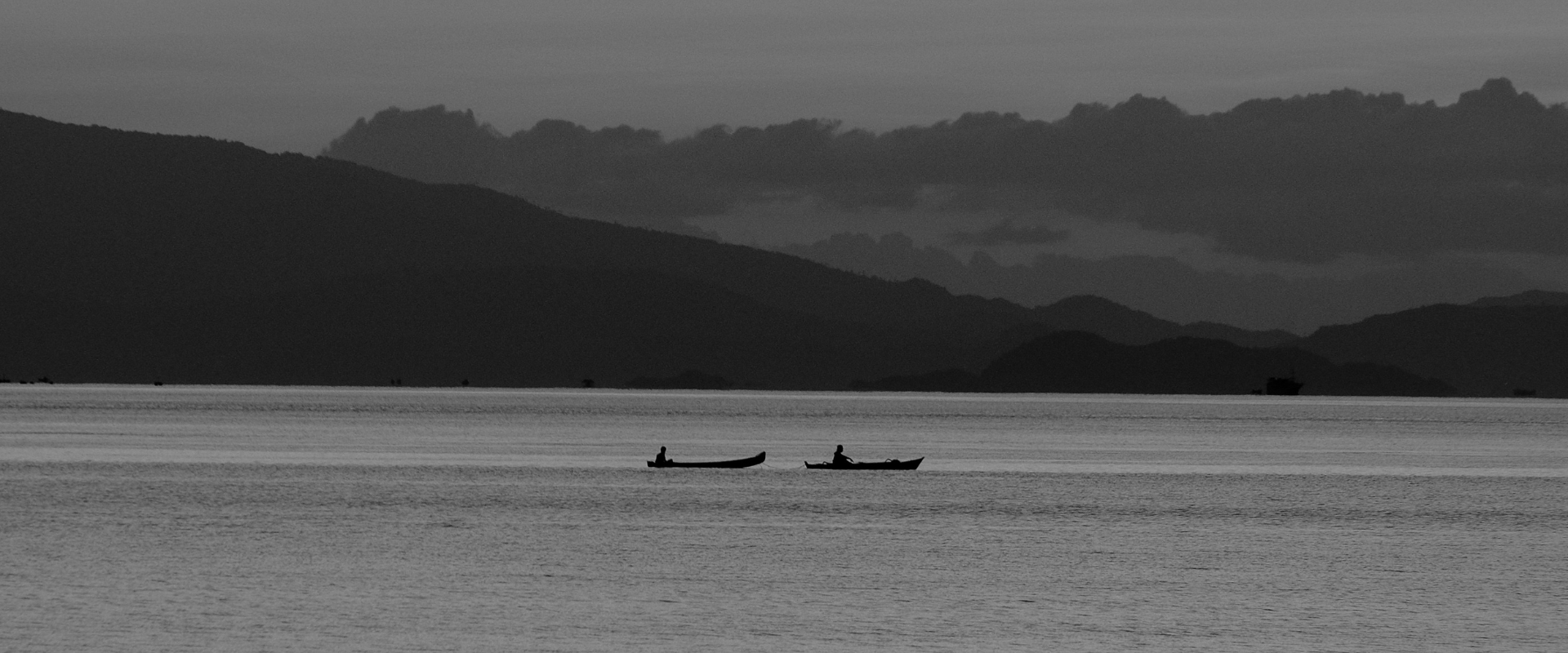 Two traditional wooden boats floating on calm water beneath a colourful sunset in Flores, Indonesia.