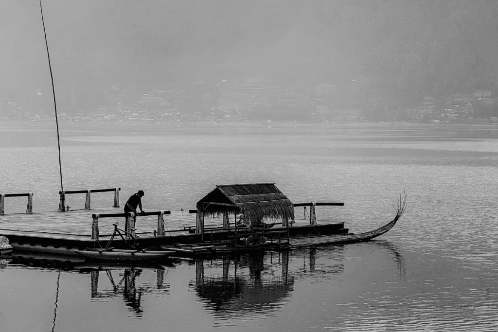 A traditional wooden platform with a thatched shelter floating on a calm lake in Bali.