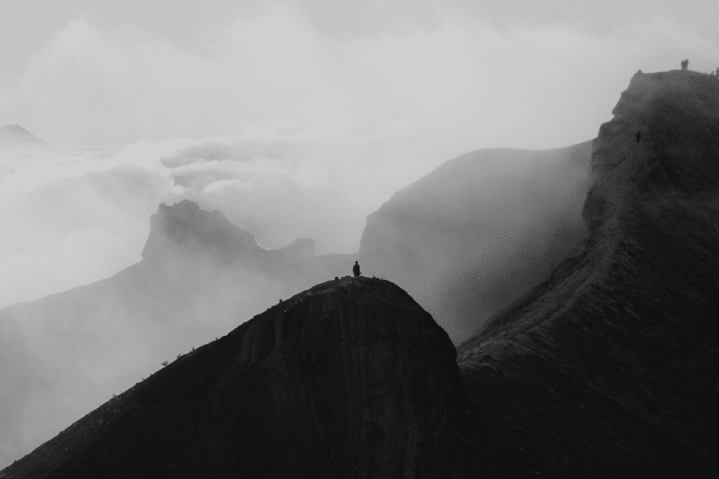A lone hiker standing on a mountain ridge above the clouds at sunrise near Mount Agung, Bali.