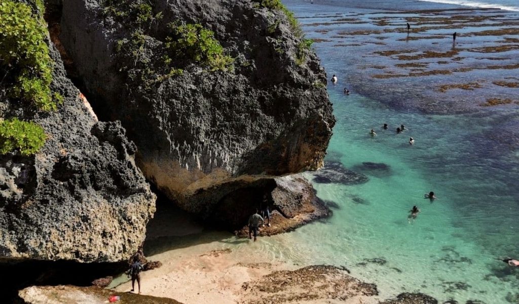 Cliffside view of Suluban Beach in Uluwatu, Bali, with turquoise waves and rugged limestone formations.