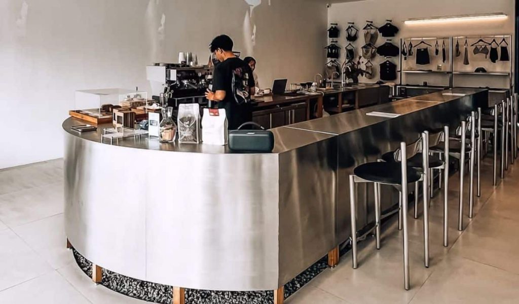 Minimal industrial interior at Projects Bali in Canggu featuring a metallic coffee bar, clean white walls, and modern design